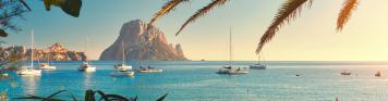 Ibiza Palmenstrand auf Ibiza mit ankernden Segelbooten im Hintergrund.